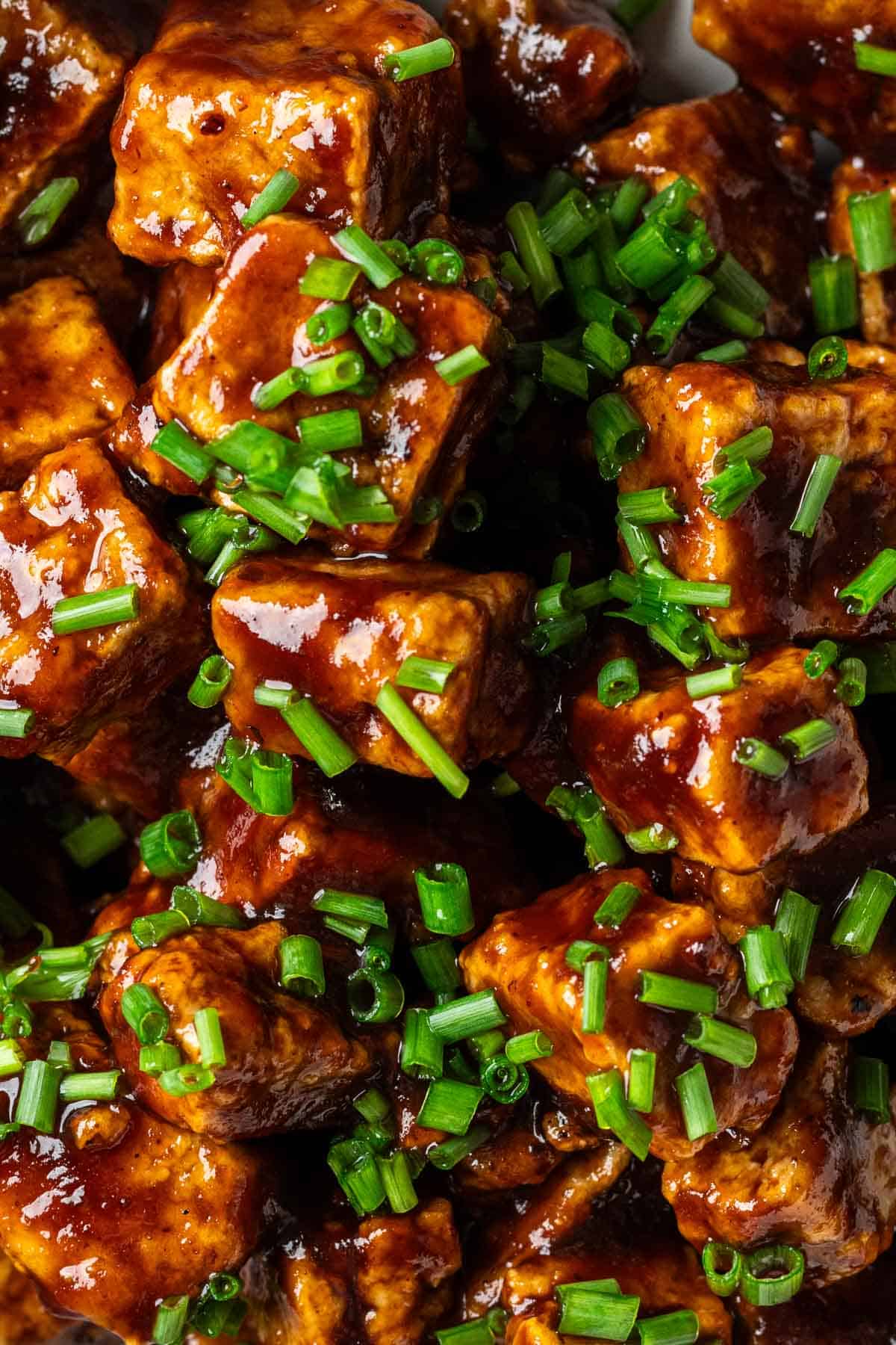 Close up of crispy tofu cubes in bbq sauce topped with chives.