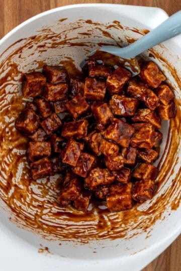 Bite sized pieces of tofu tossed in bbq sauce in mixing bowl.