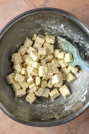 Cubed tofu coated in cornstarch and spices in a mixing bowl before being cooked.