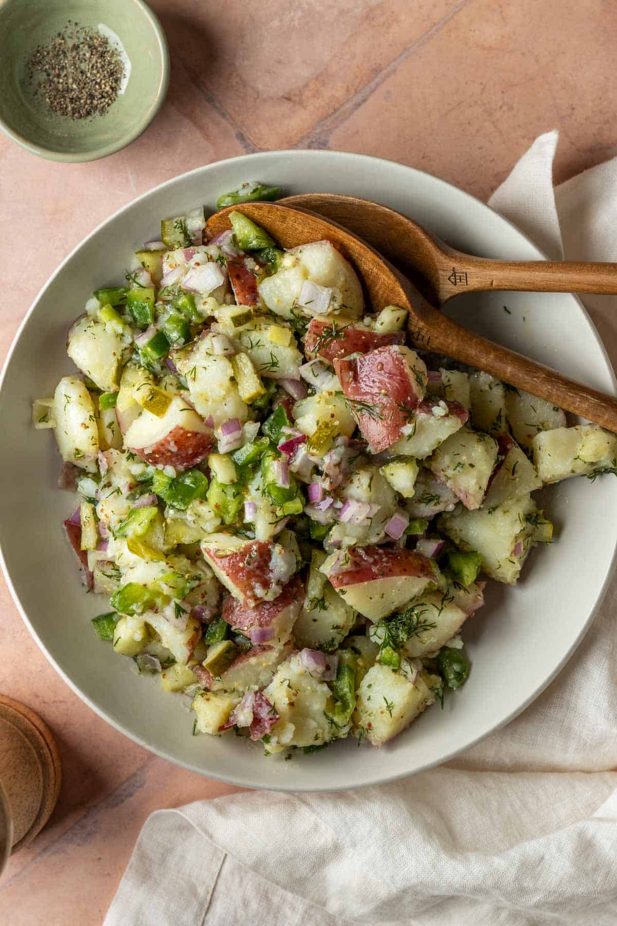 A large bowl of dill pickle potato salad being served with wooden utensils.