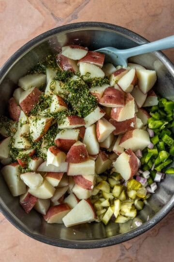 Potatoes, peppers, onions, pickles and dressing in a bowl.