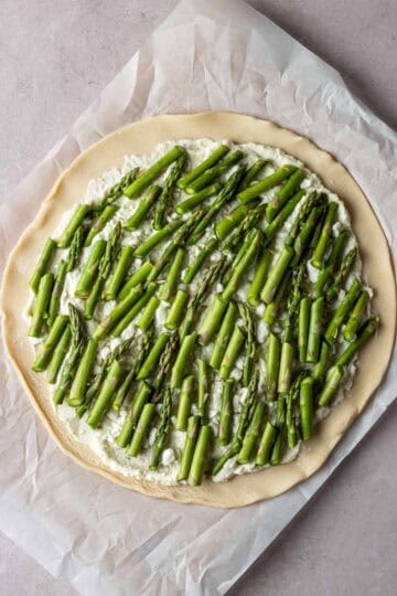 Rolled out pie crust topped with cheese and sliced asparagus.