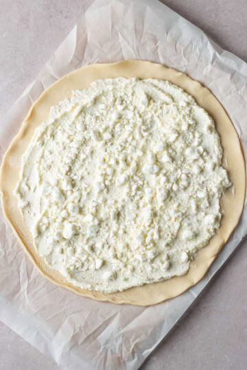 A rolled out pie crust topped with ricotta cheese and goat cheese.