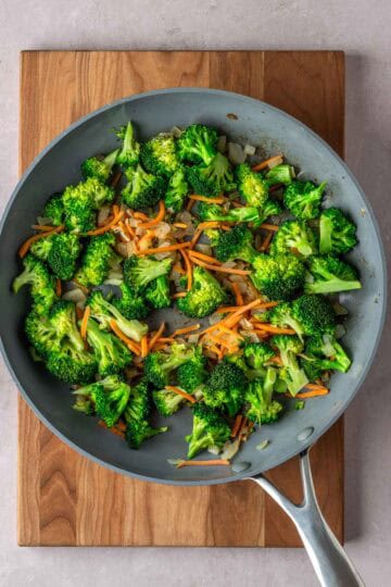 Sautéed broccoli, carrots and onions in a pan.