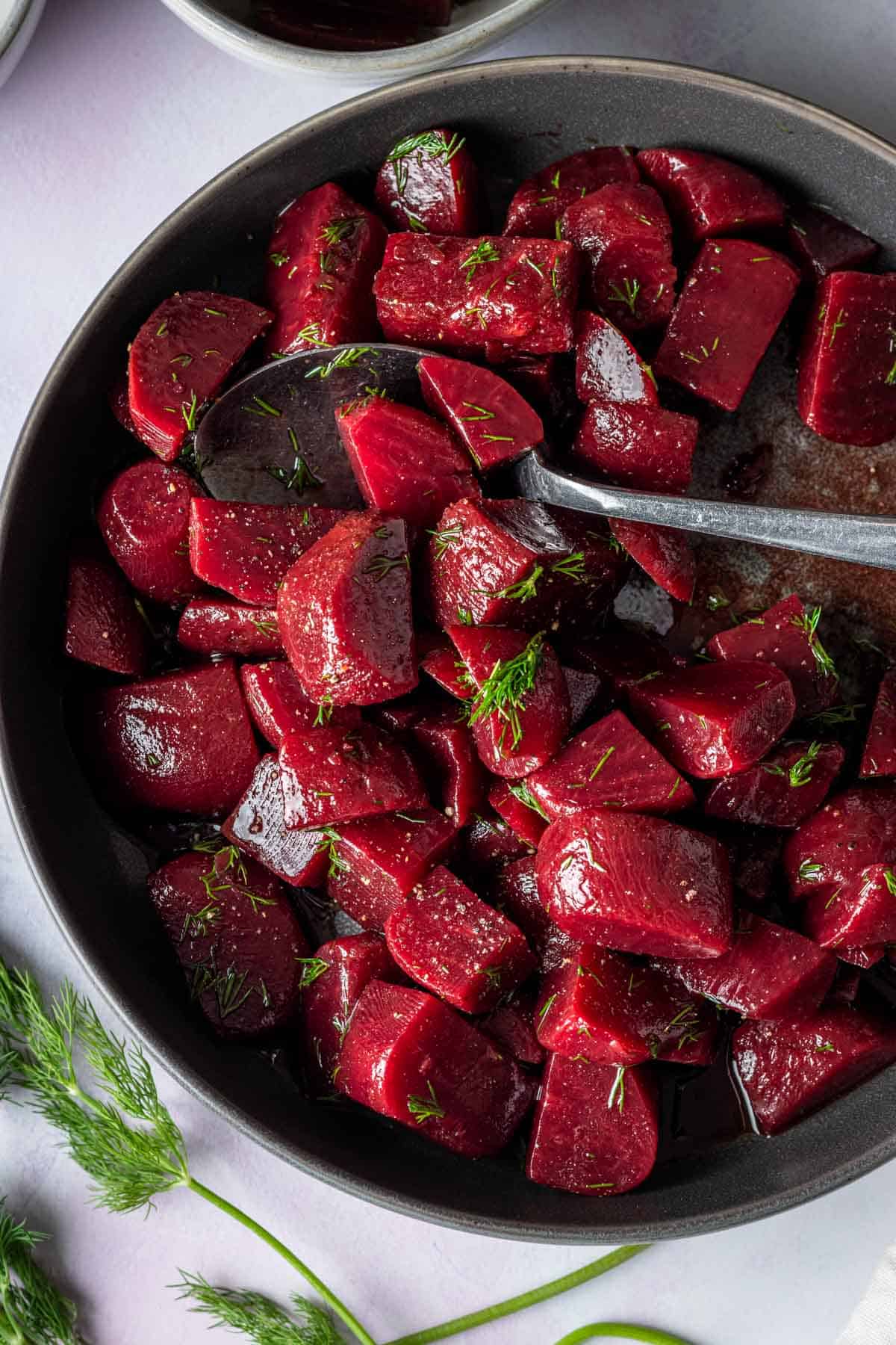 Pickled beet salad in a dark grey bowl topped with fresh dill.
