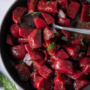 Pickled beet salad in a dark grey bowl with a spoon topped with fresh dill.