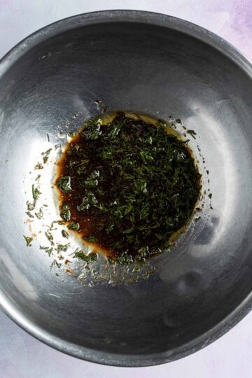 Vinegar, oil and fresh herbs in a mixing bowl.
