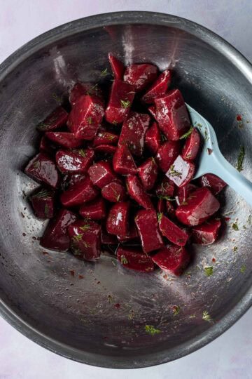A large mixing bowl with cooked beets tossed in dressing.